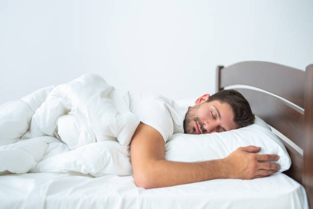 The handsome man sleeping on the bed on the white background stock photo