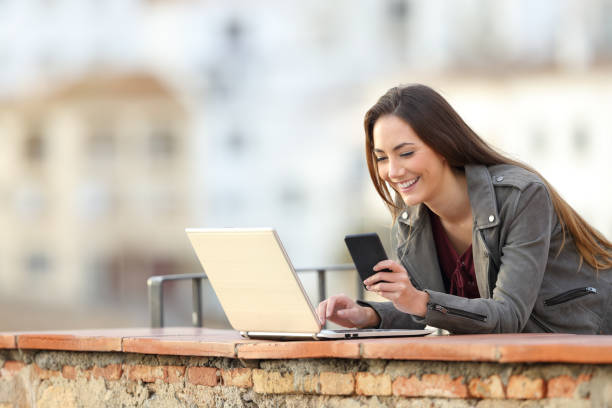 istock Happy woman using phone and laptop in a balcony 1077193980