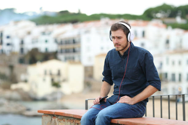 Sad man listening to music on a ledge