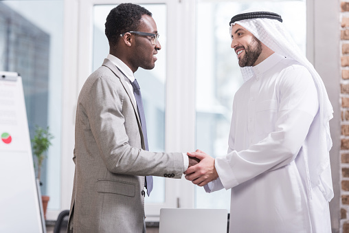 Multicultural businessmen smiling and shaking hands in modern office