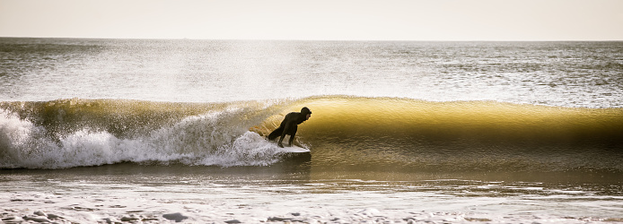 Surfer rides a wave on the New Jersey coast on a cold November morning. The cold weather doesn't stop the avid surfer thanks to the wetsuit. New Jersey has 130 miles of beaches offering many recreational activities in addition to surfing.