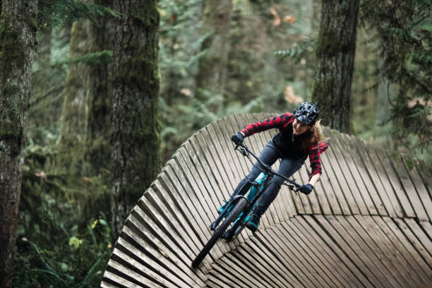 Woman Mountain Biking On Forest Trails An adult woman takes a large wooden berm ramp corner, a smile and look of exhilaration on her face.  Shot in the Pacific Northwest, Issaquah, Washington, USA. hard and fast stock pictures, royalty-free photos & images