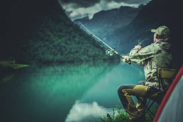Glacial Lake Fly Fishing. Caucasian Fisherman on a Lake Shore.