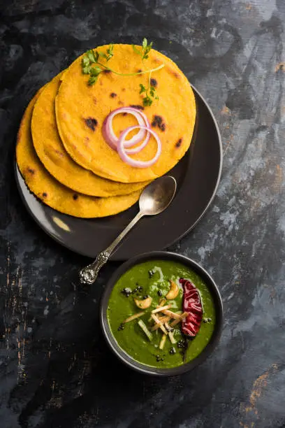 Photo of Makki di roti with sarson ka saag, popular punjabi main course recipe in winters made using corn breads mustard leaves curry. served over moody background. selective focus