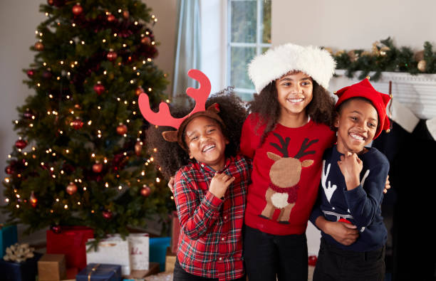 Portrait Of Children Wearing Festive Jumpers And Hats Celebrating Christmas At Home Together Portrait Of Children Wearing Festive Jumpers And Hats Celebrating Christmas At Home Together brother photos stock pictures, royalty-free photos & images
