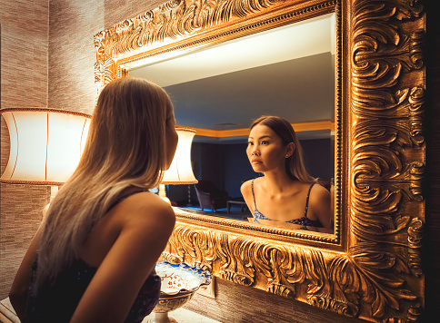 Asian woman checking herself out in a luxury mirror at five stars hotel room