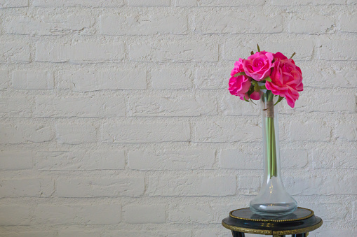Pink roses in a glass vase isolated on a white brick wall, valentines day or interior background