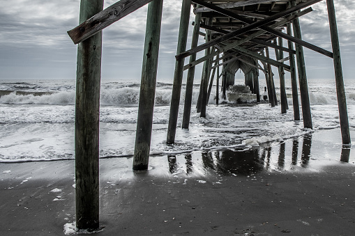 Waves crashing under a wooden pier at the beach