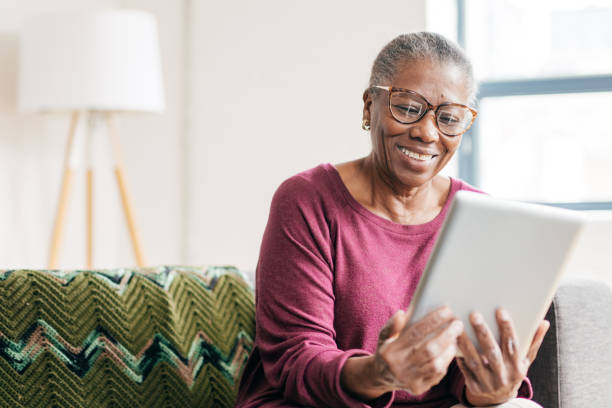 senior femenino en casa usando la tableta - surfista de plata fotografías e imágenes de stock