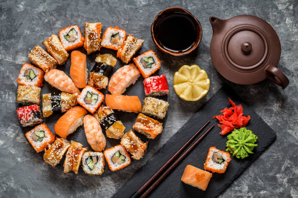 istock sushi rolls on round slate black Board with wasabi and ginger, soy sauce on grey background 1077248220