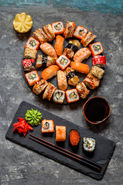 istock sushi rolls on round slate black Board with wasabi and ginger, soy sauce on grey background 1077248496