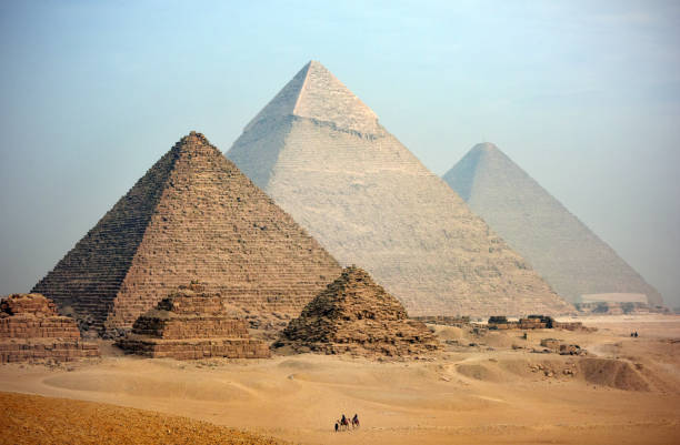 Pyramids A distant camel caravan passes the majestic pyramids at Giza in Cairo at dusk. Egypt great pyramid of khufu stock pictures, royalty-free photos & images