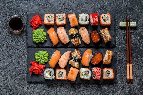 istock sushi rolls Asian food on rectangular shale plates with wasabi and ginger, soy sauce on dark background 1077252072