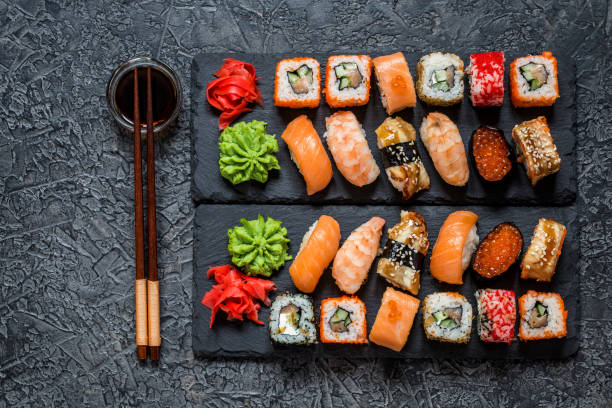 istock sushi rolls Asian food on rectangular shale plates with wasabi and ginger, soy sauce on dark background 1077252082