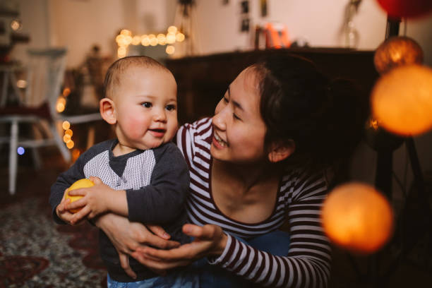 Brightly lit image of a young Thai mom with her little baby boy. They're spending time together at home, playing with toys. Asian family lifestyle concepts, shot in Europe.