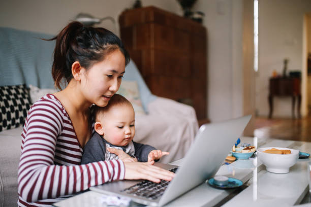 Young Asian mom trying to work with her baby boy Portrait of a young Asian woman sitting at home, doing some freelance job while taking care of her little baby boy. Home living and lifestyle concepts with Asian people. asian ethnicity family stock pictures, royalty-free photos & images