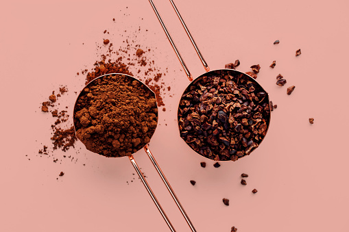 Rose gold measuring cups of cacao nips and cocoa powder on a pink background, flat lay healthy food concept
