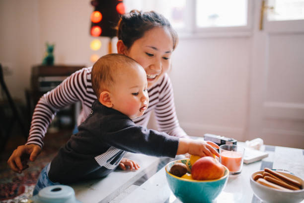 joven mamá asiática dando alimento a su bebé - child eating healthy eating healthy lifestyle fotografías e imágenes de stock