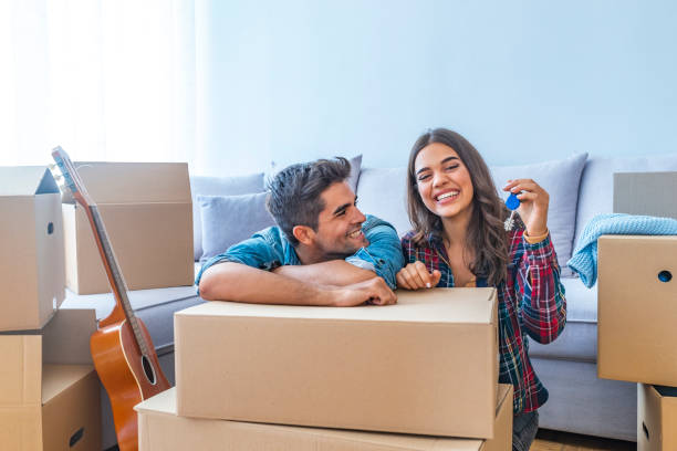 Happy couple holding keys to new home Cheerful and happy young couple holding the keys of their new home with moving cardbox during move into new apartment. Happy couple holding keys to new home. Couple celebrating moving to new home key package stock pictures, royalty-free photos & images