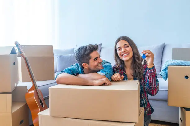 Cheerful and happy young couple holding the keys of their new home with moving cardbox during move into new apartment. Happy couple holding keys to new home. Couple celebrating moving to new home
