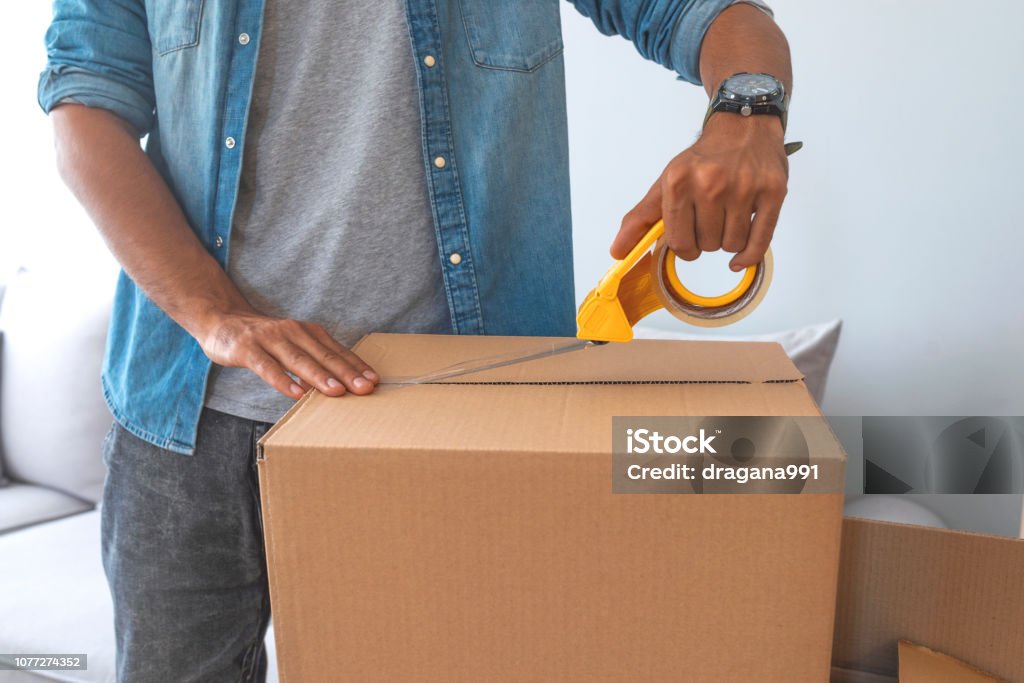 House moving concept Close up of male hand packing cardboard box, concept moving house. House moving concept. Happy young couple moving into new apartment with packaging boxes. Male hands packing cardboard box with scotch Box - Container Stock Photo