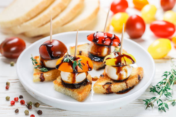 istock Bread toast with tomato cherry, mozzarella cheese, thyme and balsamic glaze on white wooden background. Canape. bruschetta. Gourmet snack. Selective focus 1077282816