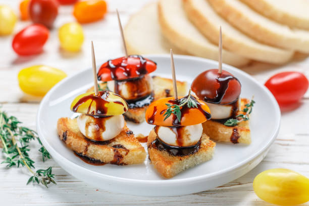 istock Bread toast with tomato cherry, mozzarella cheese, thyme and balsamic glaze on white wooden background. Canape. bruschetta. Gourmet snack. Selective focus 1077282818