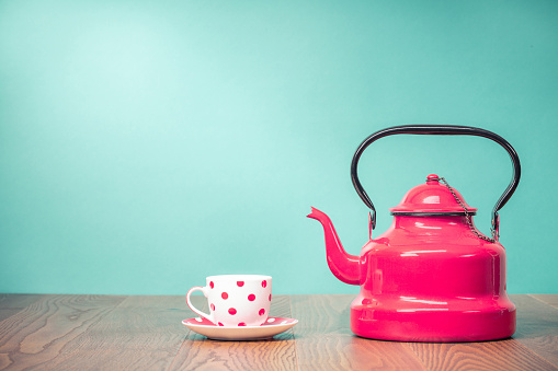 Retro classic red kettle and cup of tea with polka dots on oak wooden table in front aquamarine wall background. Vintage old style filtered photo