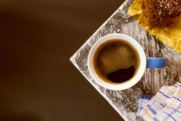 Photo of Chocolate brownie sprinkled with cocoa and coconut in the background with a coffee mug on the corner of a table near a window.