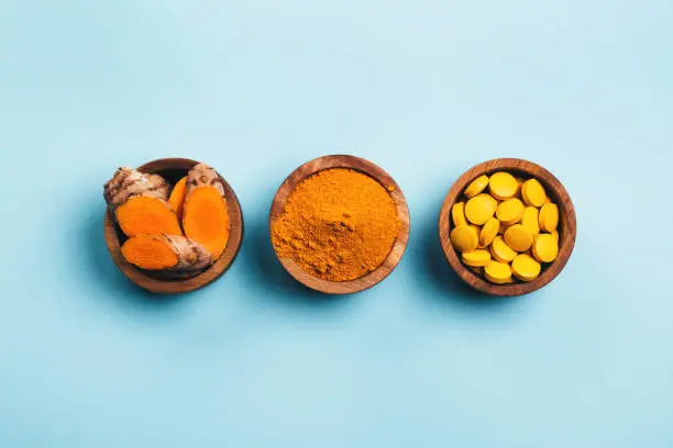 Turmeric in different conditions: fresh, dry root, pills, powder and cut plant on pastel blue background. Flat lay style.
