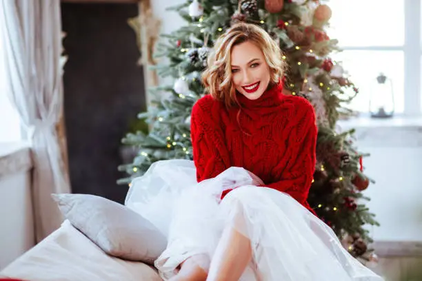 Photo of smiling woman in red sweater over christmas tree background