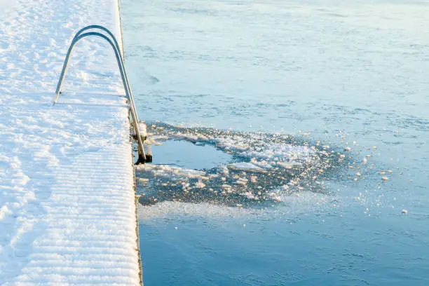 Photo of Ladder at lake footbridge. Fresh ice hole for swimming. Cold day. Care about body health in winter time. Side view.