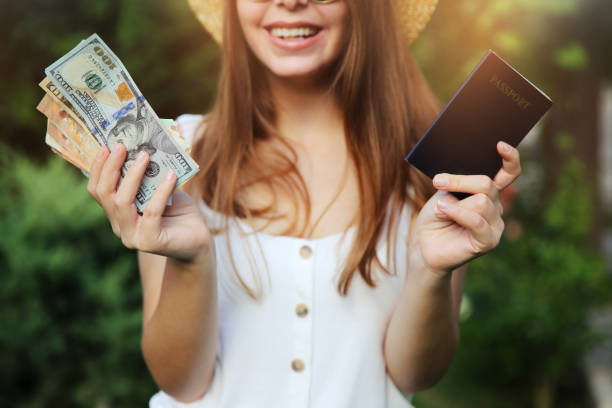 Portrait of cheerful, happy, pretty, charming, laughing girl  with hat on head, having money fan and passport with tickets in raised hands stock photo
