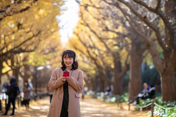 młoda kobieta słuchająca muzyki pod drzewami ginkgo - ginkgo tree ginkgo tree japan zdjęcia i obrazy z banku zdjęć