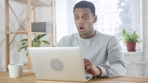 istock Shocked, Wondering Afro-American Man Working on Laptop, Sitting at Office 1077357618
