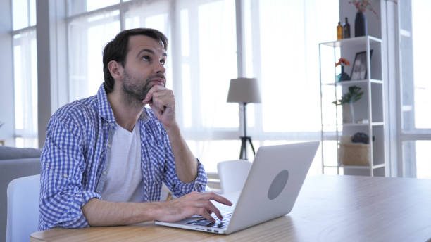 istock Pensive Casual Beard Man Thinking and Working on Laptop 1077359982