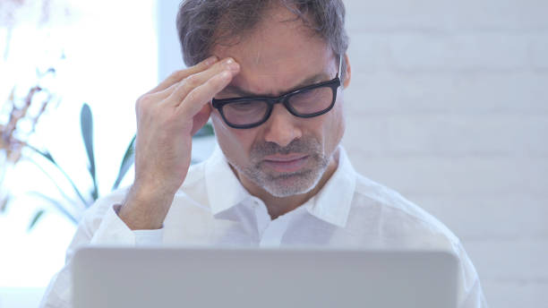 istock Headache, Upset  Middle Aged Man working in Office Close Up 1077360158