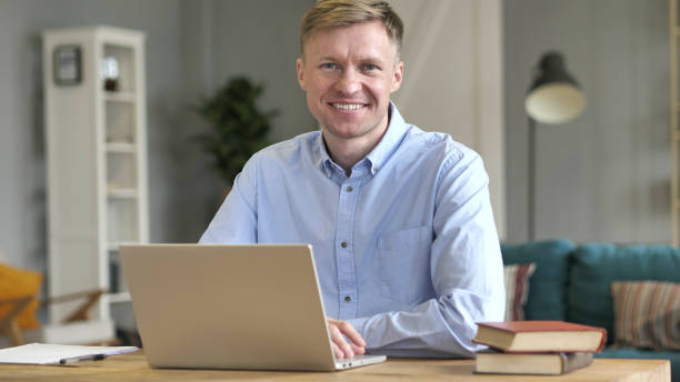 istock Smiling Businessman Looking at Camera while Working on Laptop 1077363910