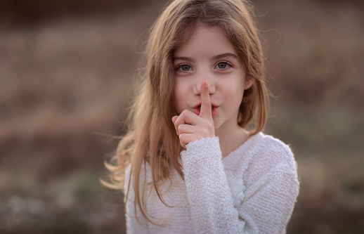 Cute child with finger on lips making a silent gesture. Shh concept, be quiet gesture
