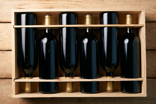 Wine bottles in wooden crate on wood table background, close-up. Red wine in wood box case in wine shop