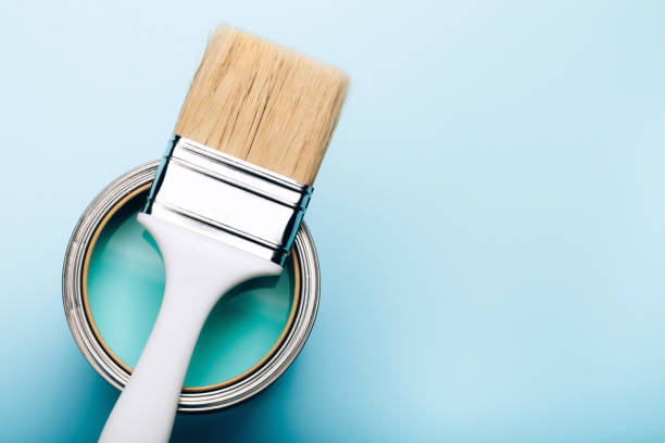 istock Brush on open can of turquoise paint on blue pastel background. 1077401644