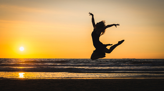Silhouette of a happy girl jumping in the beach at the sunset. Freedom and leisure vacation concept.