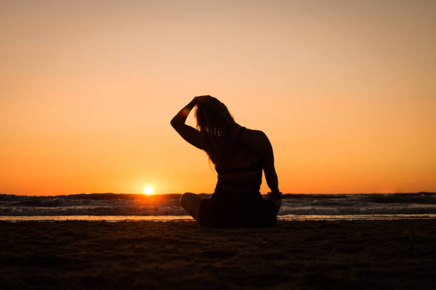 Silhouette of a girl practicing yoga on the beach at sunset