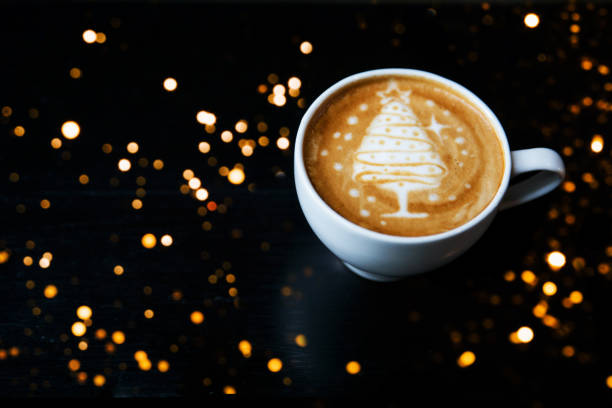 Tasty cappuccino with Christmas tree latte art with some blurred lights. Holiday concept.