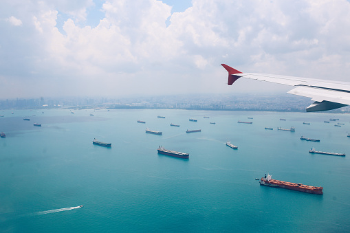 Airplane landing in Singapore, flying above the fleet of nautical vessels.