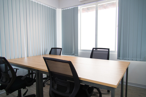 Modern meeting room of business company. Wooden table and four chairs around near window with curtains. Office interior concept