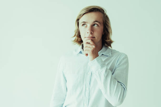 Dreamy young man touching chin and looking away. Attractive guy dreaming. Dream concept. Isolated front view on white background.