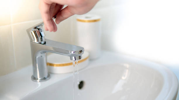 Male hand opening water tap or faucet in bathroom. Save water at home or water conservation concepts stock photo