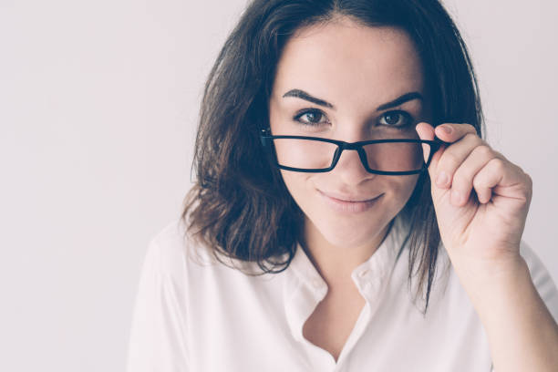 Joyful smiling girl removing glasses. Young Caucasian woman peeking over eyeglasses. Vision correction and eye care concept