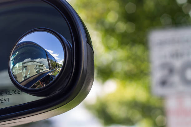 A curved traffic safety mirror mounted outdoors shows the reflection of a yellow school bus against a backdrop of lush green trees and foliage.